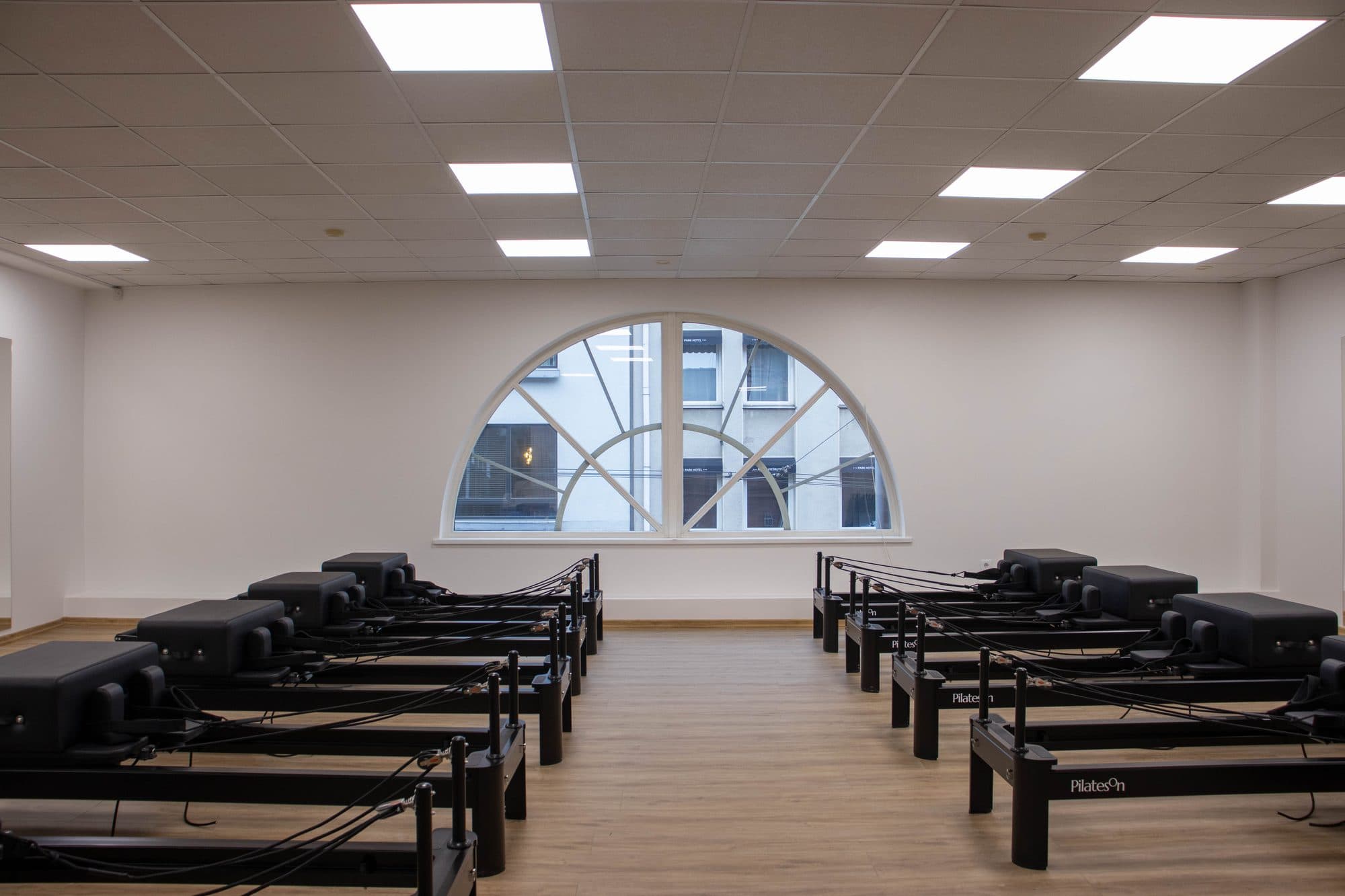 Bright, symmetric PilatesOn reformer room with rows of branded reformer beds facing a half-moon window